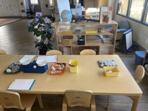 A table with various science items, such as a balance, rocks, and shells. Three clipboards with papers as well as a container with pencils are also visible.